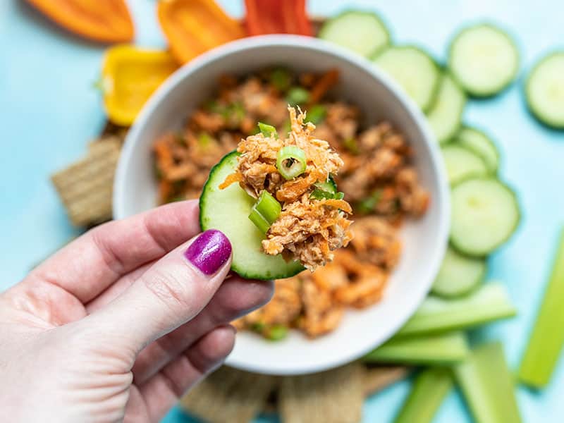 This Sweet and Spicy Tuna Salad is bold and flavorful, and has no mayonnaise! It's the perfect quick fix for summer months or your weekly meal prep. BudgetBytes.com Close up view of Sweet and Spicy Tuna Salad on a slice of cucumber, the bowl in the background.