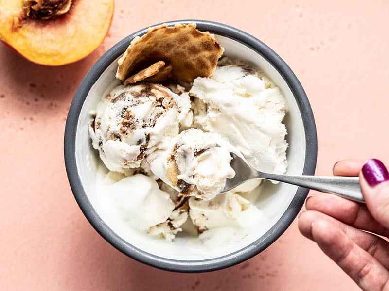 This No Churn Balsamic Peach Ice Cream is incredibly easy and pairs the flavor of fresh sweet summer peaches with a tangy and buttery balsamic glaze. BudgetBytes.com A hand lifting a spoonful of No Churn Balsamic Peach Ice Cream out of the bowl