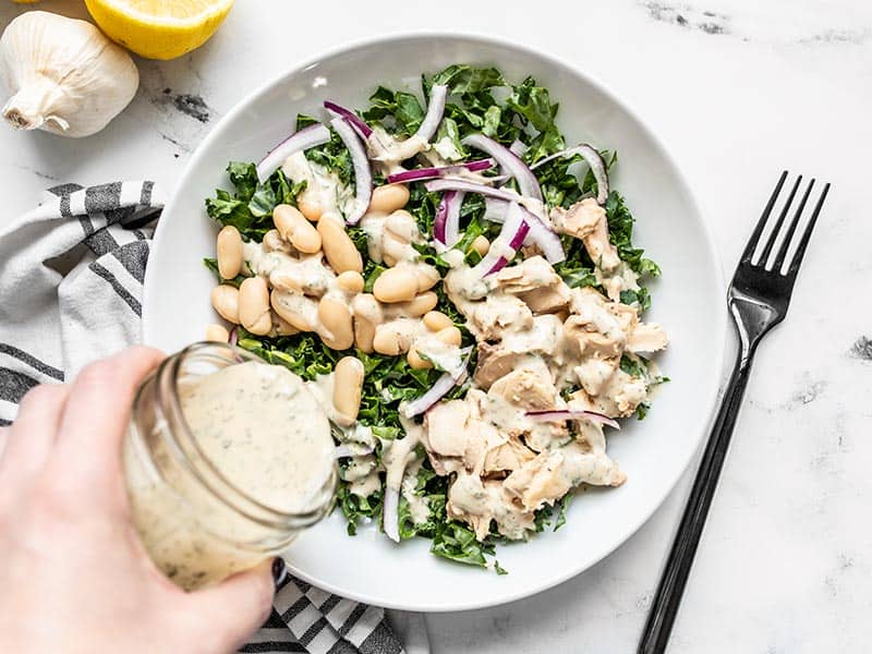 This super simple Lemon Dill Salmon and Kale Salad is a fast, convenient, and filling lunch for hot summer days when it's too hot to cook. BudgetBytes.com Lemon Dill Tahini Dressing being drizzled over a salmon and kale salad