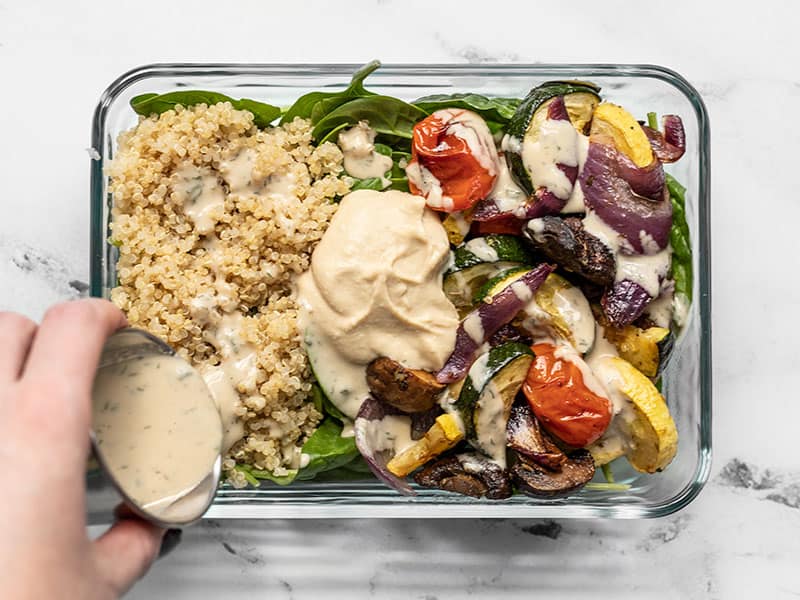 These Roasted Vegetable Salad Meal Prep boxes are an easy, no-reheat, plan-ahead lunch option that will help you get your daily vegetables! BudgetBytes.com Dressing being poured onto a Roasted Vegetable Salad Meal Prep container