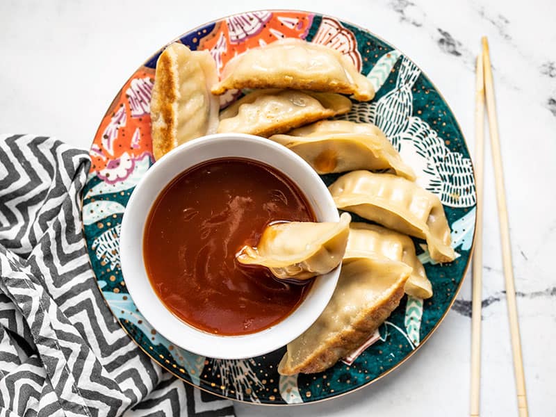 This Simple Sweet and Sour Sauce can be whipped up in minutes with only a few pantry staples, so you don't have to keep another condiment in your fridge! BudgetBytes.com A dumpling sitting in a bowl of sweet and sour sauce, on a plate full of dumplings.