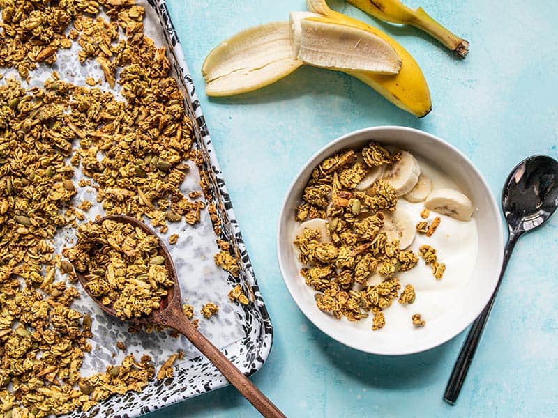 Aquafaba (the leftover starchy water from canned beans) makes this Oil Free Granola super crunchy without using excessive amounts of oil and sugar! BudgetBytes.com A sheet pan of Super Crunchy Oil Free Granola next to a bowl with yogurt and granola, and a half eaten banana.