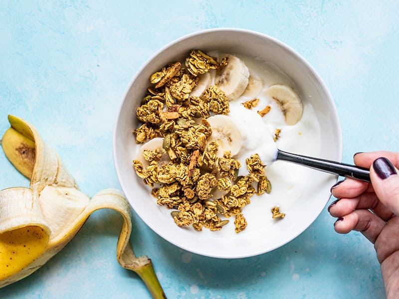 Aquafaba (the leftover starchy water from canned beans) makes this Oil Free Granola super crunchy without using excessive amounts of oil and sugar! BudgetBytes.com A bowl of yogurt with banana slices and Super Crunchy Oil Free Granola