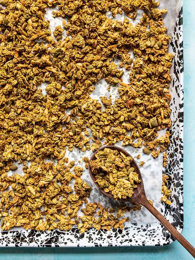Aquafaba (the leftover starchy water from canned beans) makes this Oil Free Granola super crunchy without using excessive amounts of oil and sugar! BudgetBytes.com Overhead view of the tray full of Super Crunchy Oil Free Granola with a wooden spoon scooping some up in the corner.