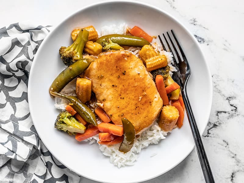 A few pantry staples are needed for these juicy Sweet and Sour Pork Chops with Vegetables, making them a quick and easy alternative to take-out. BudgetBytes.com A plate with rice and sweet and sour pork chops with vegetables, a black fork on the side of the plate.