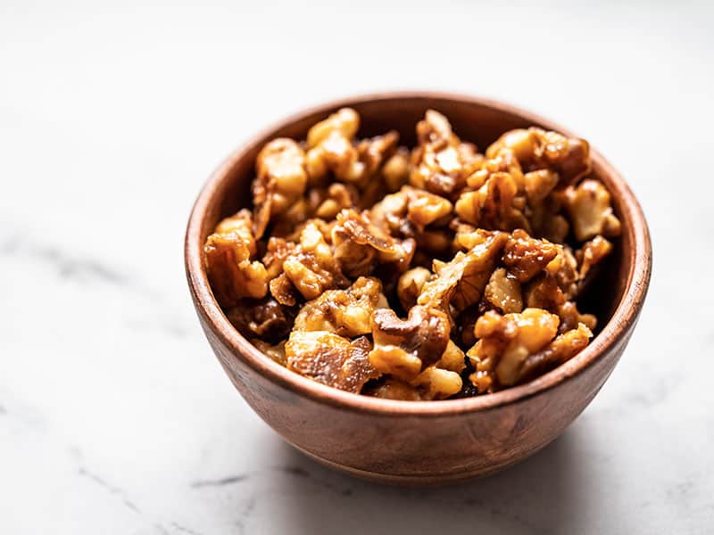 A small wooden bowl of crunchy candied walnuts from the side.