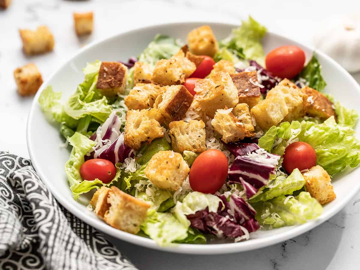 Homemade croutons are a super easy to make, and their crispy, crunchy texture takes any soup or salad to the next level! Only five ingredients! BudgetBytes.com Side view of a shallow bowl with salad topped with homemade croutons.