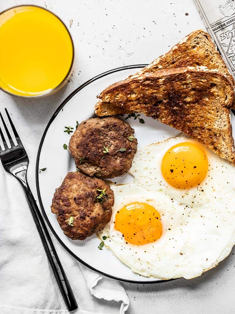 Maple Sage Breakfast Sausage is an easy way to make your weekend breakfast a little extra special, or to meal prep your breakfast protein for the week! BudgetBytes.com Two maple sage breakfast sausage patties on a plate with eggs and toast, and a glass of orange juice on the side.