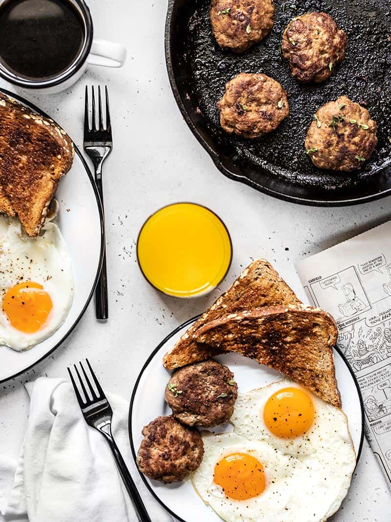 Maple Sage Breakfast Sausage is an easy way to make your weekend breakfast a little extra special, or to meal prep your breakfast protein for the week! BudgetBytes.com Tablescape with two plates full of eggs, toast, and maple sage breakfast sausage, a cast iron skillet with sausage, and drinks