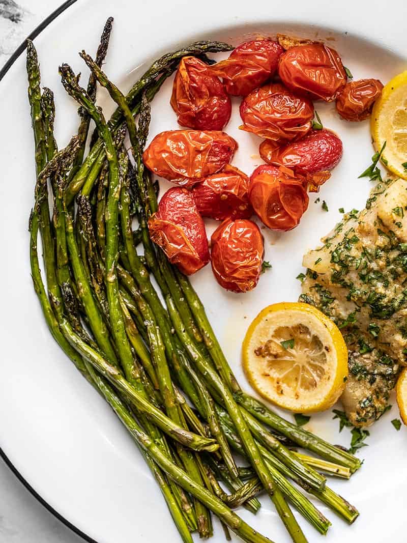 Roasted Asparagus and Tomatoes is an easy, all-purpose side dish that pairs great with many main dishes, like meat, fish, pasta, and more. BudgetBytes.com Close up of Roasted Asparagus and Tomatoes on a dinner plate.