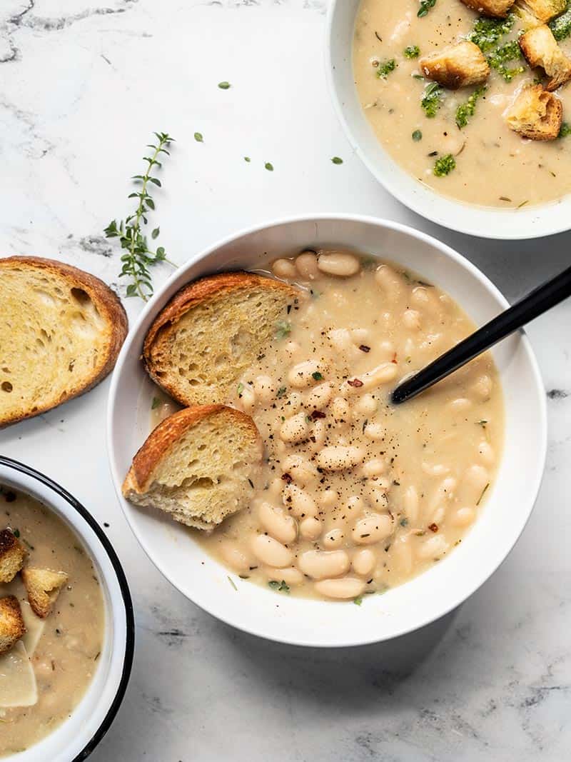 This incredibly easy Rosemary Garlic White Bean Soup takes only eight simple ingredients to deliver a bowl full of rich, bold flavor. BudgetBytes.com Three bowls of Rosemary Garlic White Bean Soup with different toppings like toasted bread, croutons, and pesto.