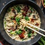 Close up overhead view of a bowl full of vegan creamy mushroom ramen with chopsticks lifting some noodles