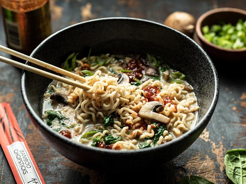 This incredibly simple Vegan Creamy Mushroom Ramen is a rich and flavorful 15 minute meal that only requires a handful of ingredients! BudgetBytes.com Front view of noodles being lifted out of a bowl of vegan creamy mushroom ramen with chopsticks