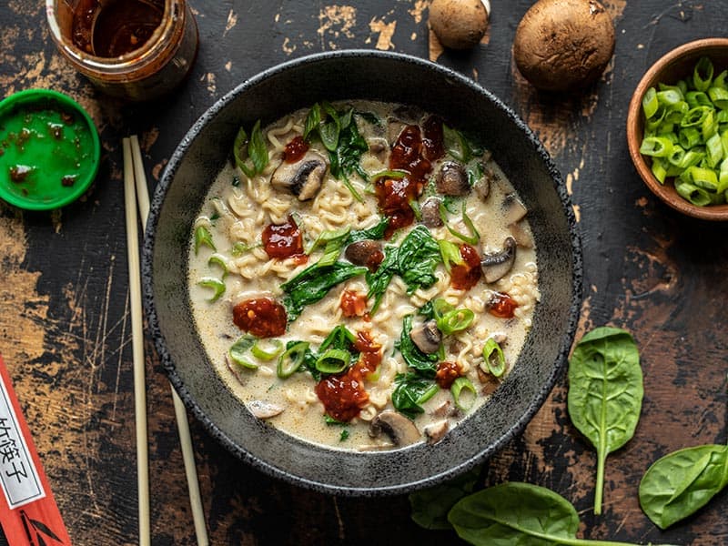 This incredibly simple Vegan Creamy Mushroom Ramen is a rich and flavorful 15 minute meal that only requires a handful of ingredients! BudgetBytes.com Overhead view of a bowl full of Vegan Creamy Mushroom Ramen garnished with chili garlic sauce and green onion