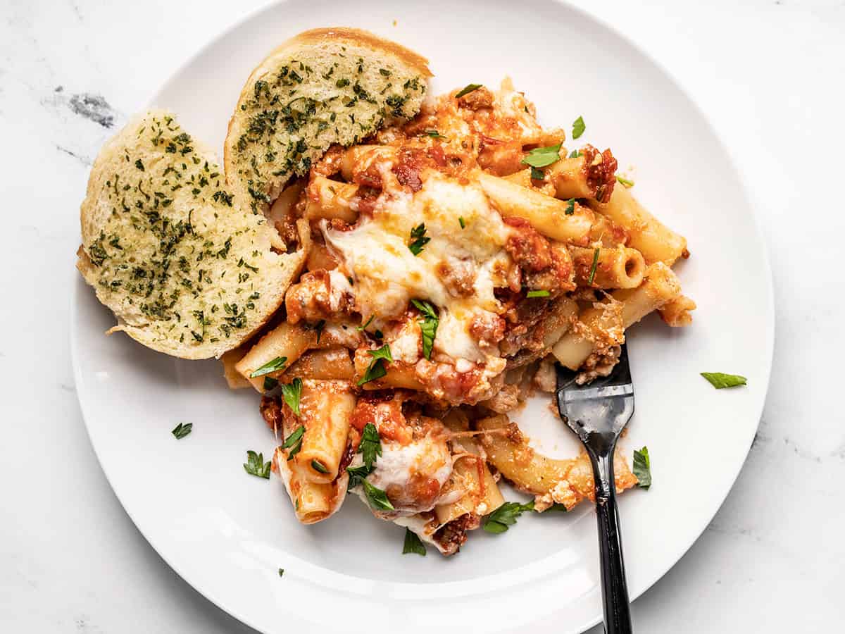 Like a freeform lasagna, this Baked Ziti has layers of pasta, homemade red sauce with Italian sausage, and three types of melty cheese! BudgetBytes.com Baked ziti on a plate with garlic bread and a fork.