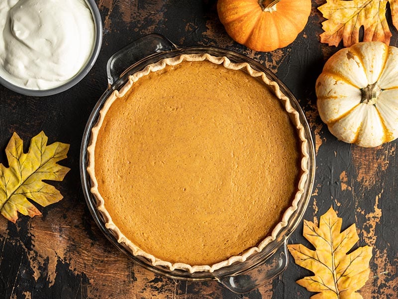 This Maple Brown Butter Pumpkin Pie is the perfect special touch for your Thanksgiving dinner, without adding a lot of extra work or unusual ingredients. BudgetBytes.com Overhead view of a baked Maple Brown Butter Pumpkin Pie, uncut with whipped cream, mini pumpkins, and leaves on the side.