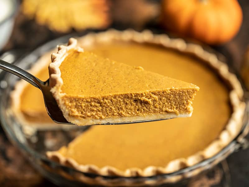This Maple Brown Butter Pumpkin Pie is the perfect special touch for your Thanksgiving dinner, without adding a lot of extra work or unusual ingredients. BudgetBytes.com A slice of Maple Brown Butter Pumpkin Pie close to the camera, whole pie in the background.