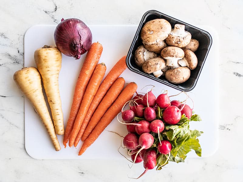 Whole vegetables for roasting on a cutting board.