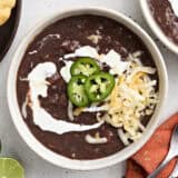 Overhead view of a bowl of black bean soup, topped with jalapeno slices, shredded cheese, and sour cream.