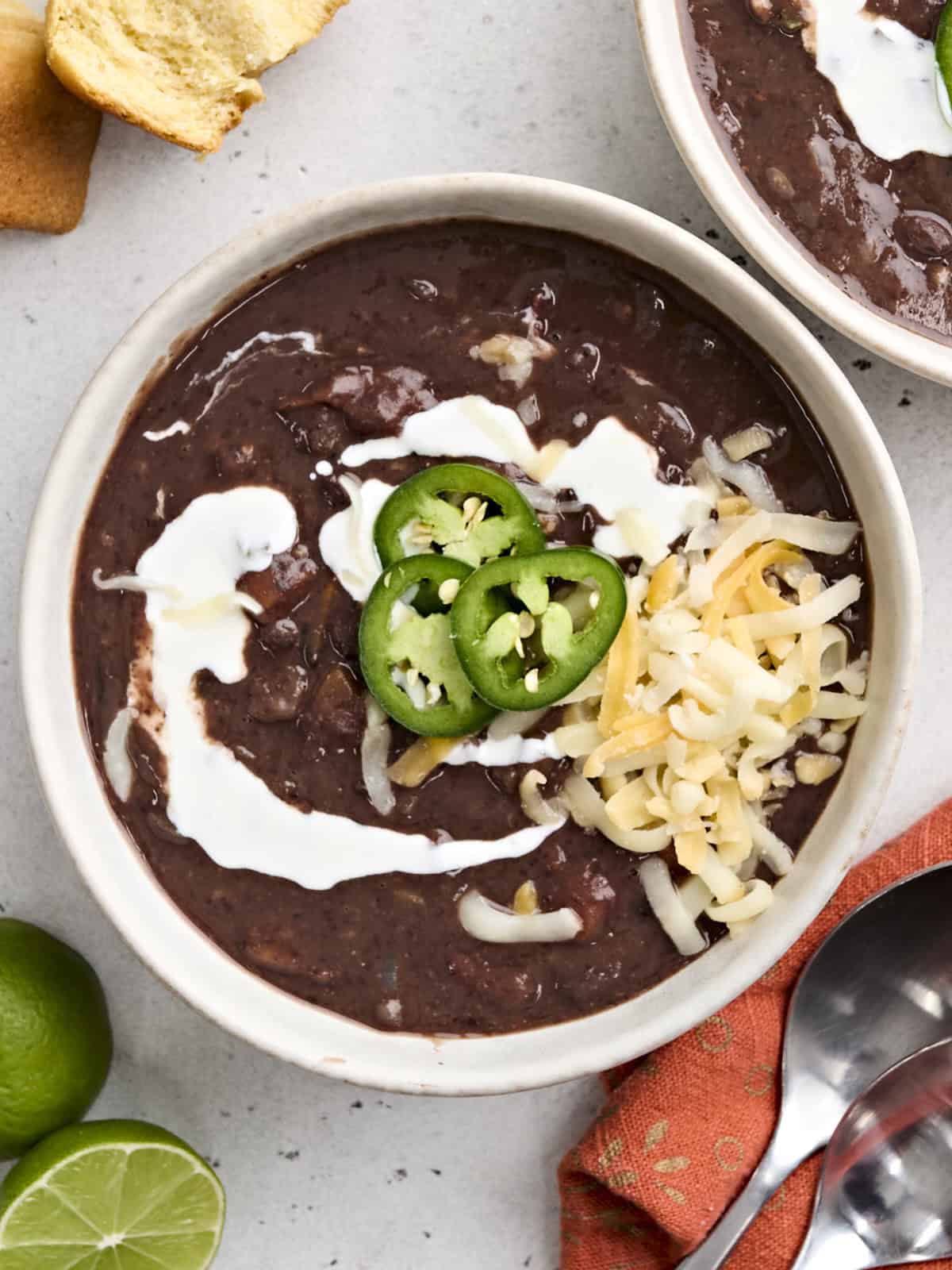 Overhead view of a bowl of black bean soup, topped with jalapeno slices, shredded cheese, and sour cream.