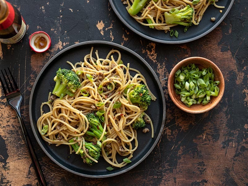 Garlic Noodles with Beef and Broccoli is a quick and easy all-in-one bowl dinner recipe with a rich, buttery, salty, and sweet sauce. BudgetBytes.com Two plates of Garlic Noodles with Beef and Broccoli next to a bottle of oyster sauce and a small bowl of sliced green onions