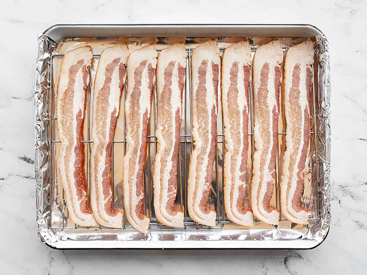 Raw bacon strips lined up on the prepared baking sheet.