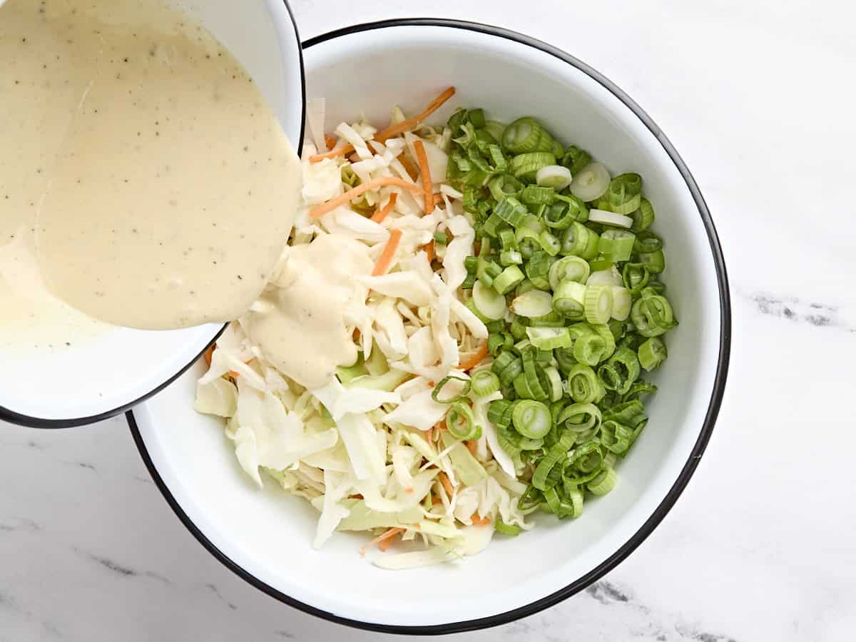 The homemade dressing being poured over shredded cabbage, carrots, and green onions to make coleslaw.