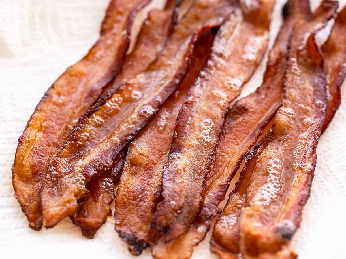 Learn how to cook bacon in the oven with very little effort and no hot splattering bacon grease! Perfect, crispy bacon in the oven every time. BudgetBytes.com Close up of oven baked bacon on a paper towel.