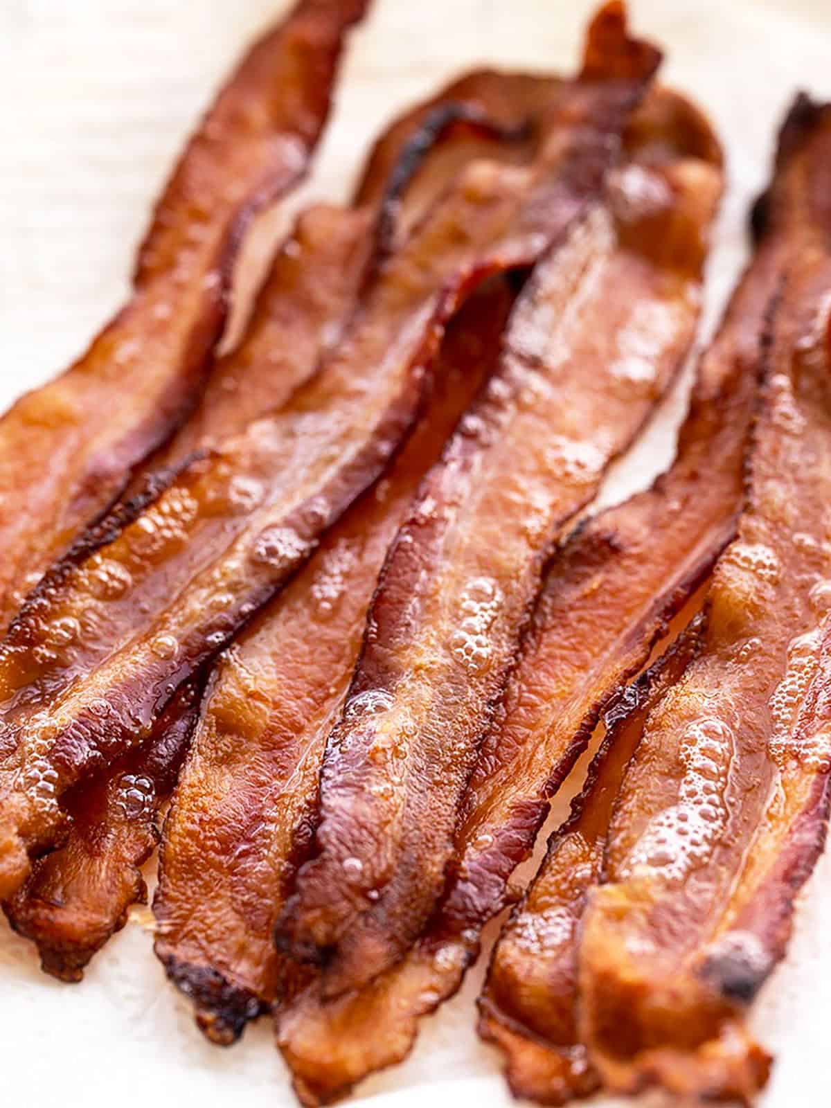 Learn how to cook bacon in the oven with very little effort and no hot splattering bacon grease! Perfect, crispy bacon in the oven every time. BudgetBytes.com Close up view of oven baked bacon strips on a paper towel lined plate.