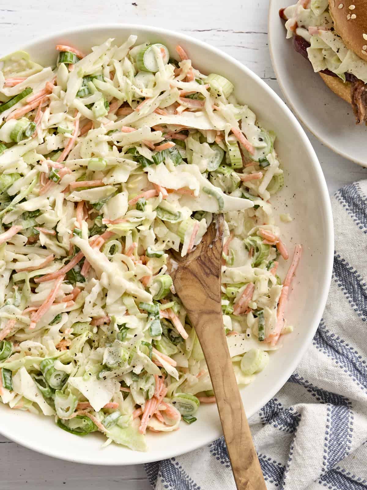 Overhead view of a bowl of coleslaw with a wooden spoon.