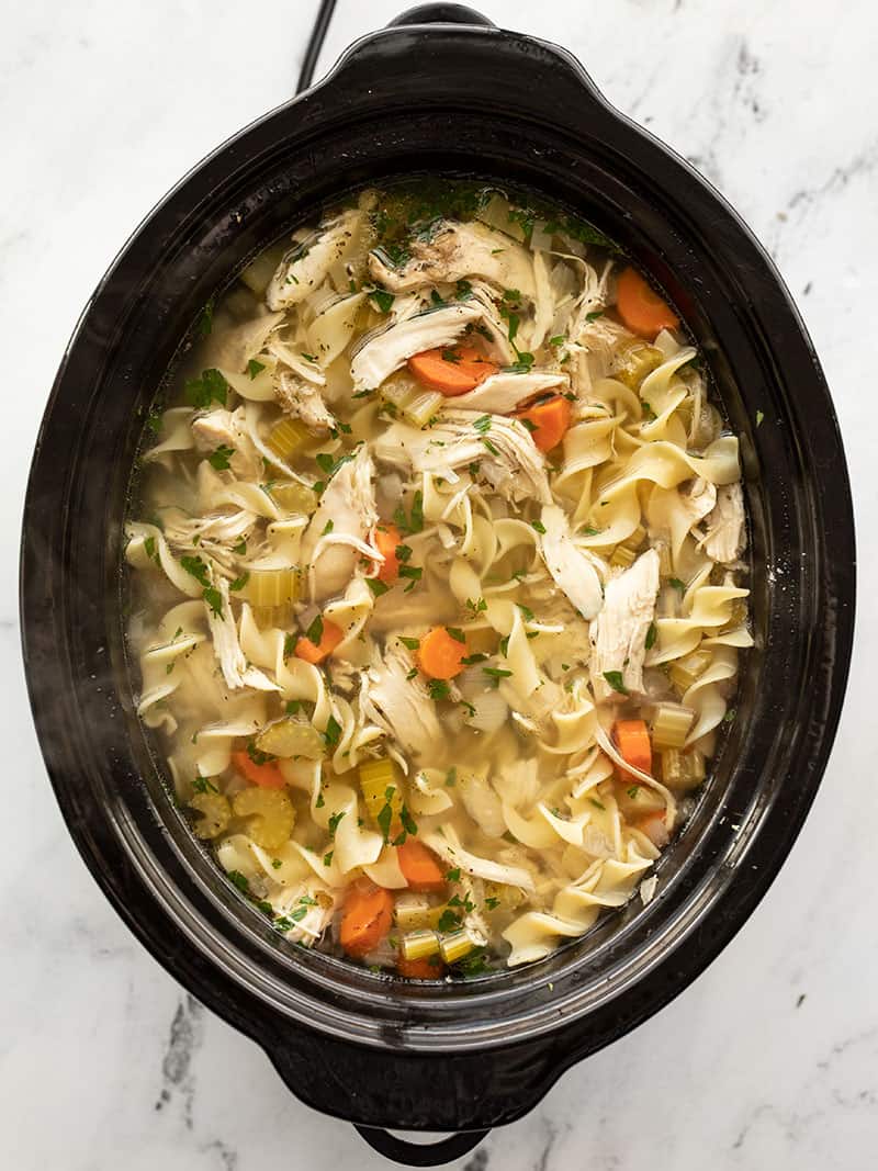 Slow cooker chicken noodle soup is an incredibly easy and soothing winter recipe that will fill you up and warm you from the inside out! BudgetBytes.com Overhead view of a slow cooker containing freshly cooked homemade chicken noodle soup