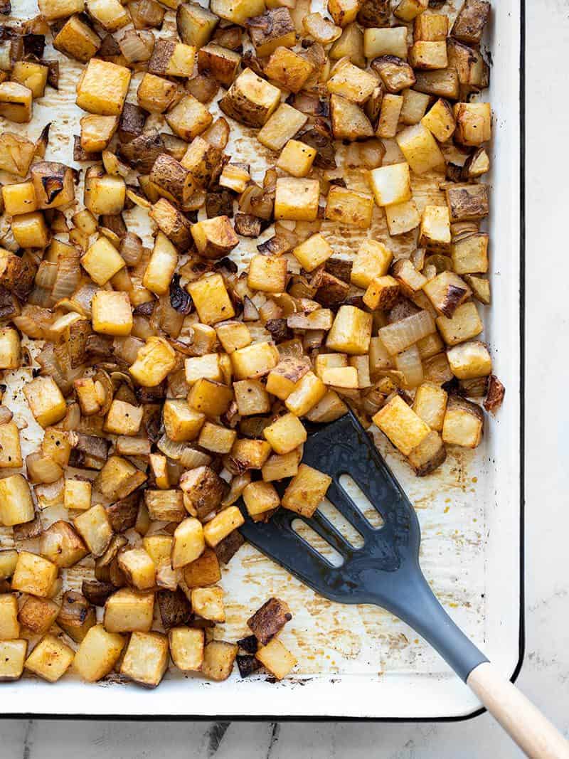 These Smoky Roasted Breakfast Potatoes cook in the oven, leaving your hands and pans free to cook your eggs and enjoy a stress-free breakfast! BudgetBytes.com A sheet pan full of roasted breakfast potatoes with onions