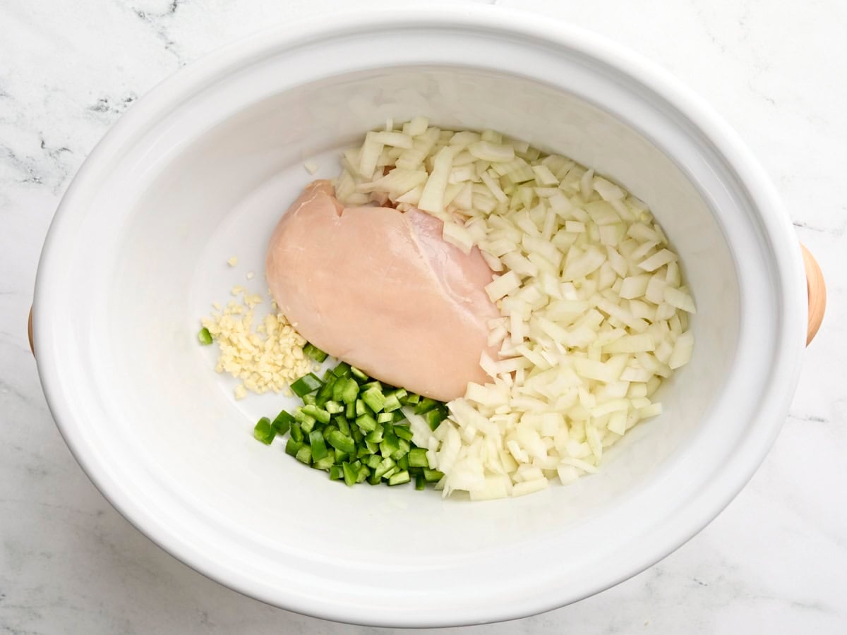 A chicken breast, minced garlic, diced onion, and jalapeno in a slow cooker.