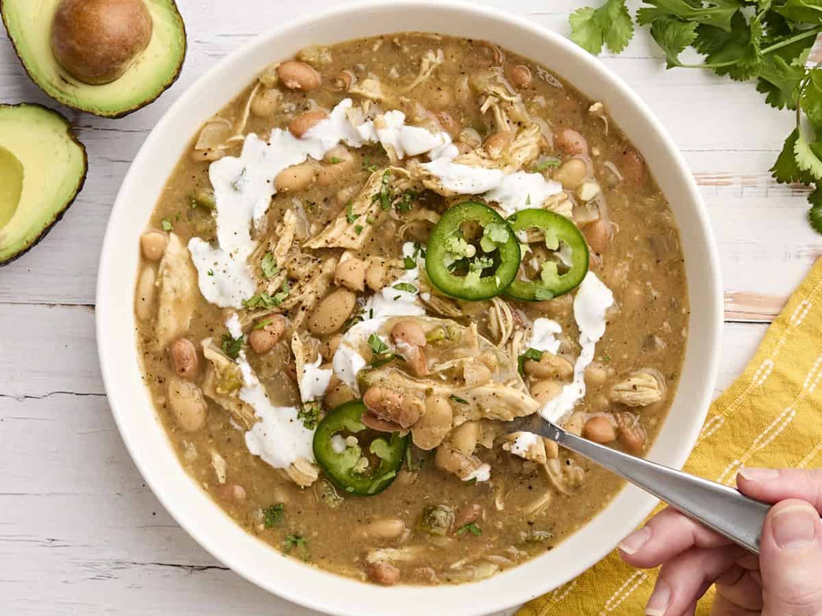 The slow cooker does all the work with this easy, flavorful, and healthy white chicken chili. This "dump and go" dinner will become a family favorite! BudgetBytes.com Crockpot white chicken chili in a bowl with a spoon taking some.