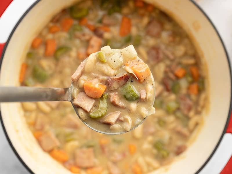 This incredibly easy and deliciously chunky Ham and Bean Soup features a medley of colorful vegetables, browned ham, and plenty of hearty white beans. BudgetBytes.com Close up of a ladle full of chunky ham and bean soup being held over the soup pot