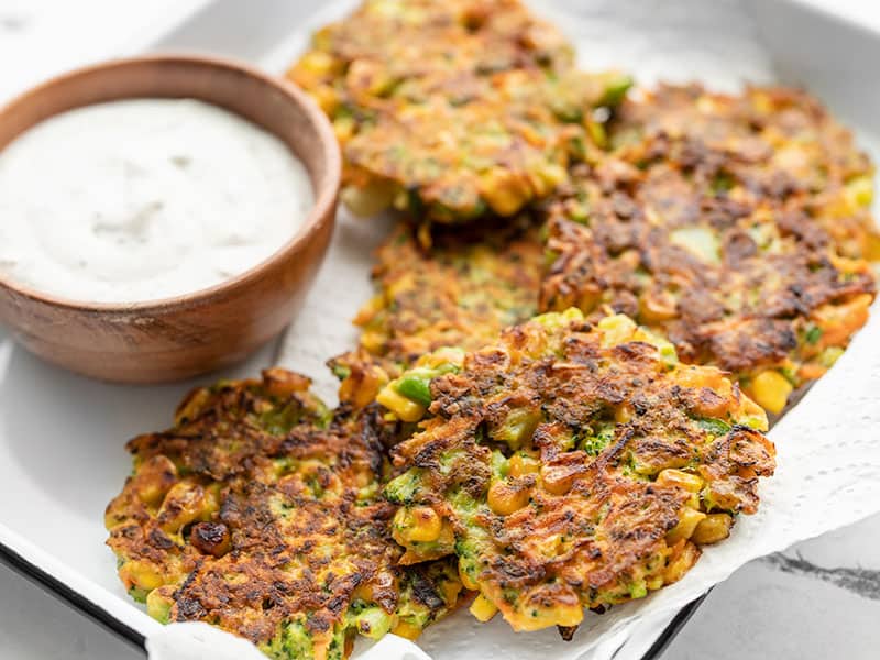 Use up your leftover frozen and fresh vegetables in this easy and flavorful vegetable fritters recipe, with a side of homemade garlic herb dipping sauce! BudgetBytes.com Front view of vegetable fritters on a tray with a small bowl of garlic herb sauce