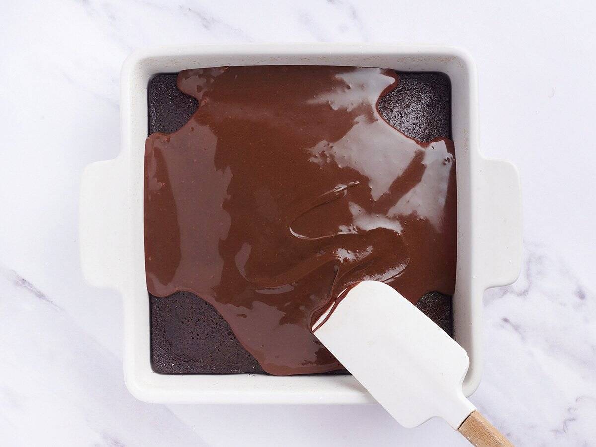 Chocolate icing being spread across a freshly baked chocolate depression cake.