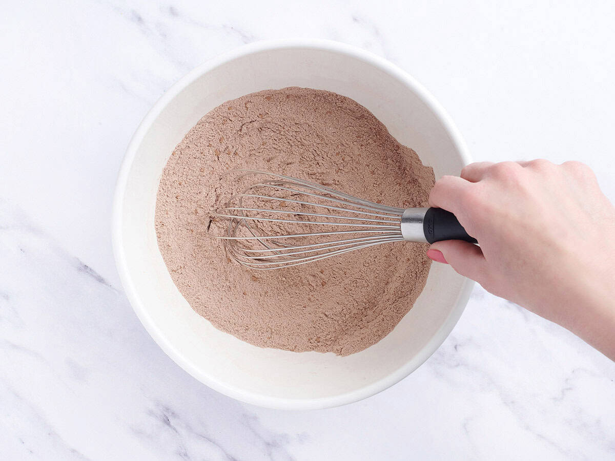 A whisk mixing the dry ingredients for chocolate depression cake in a bowl.