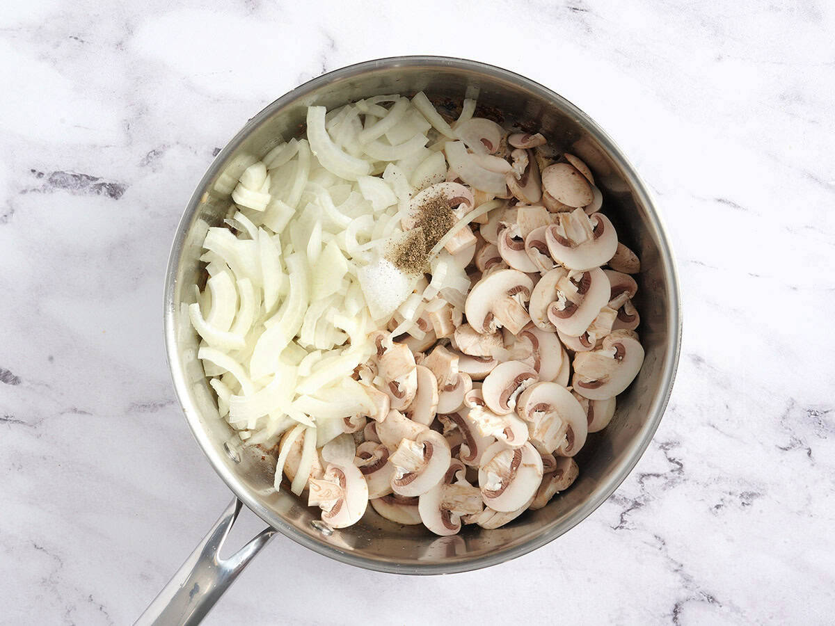Sliced onions and mushrooms in a skillet.