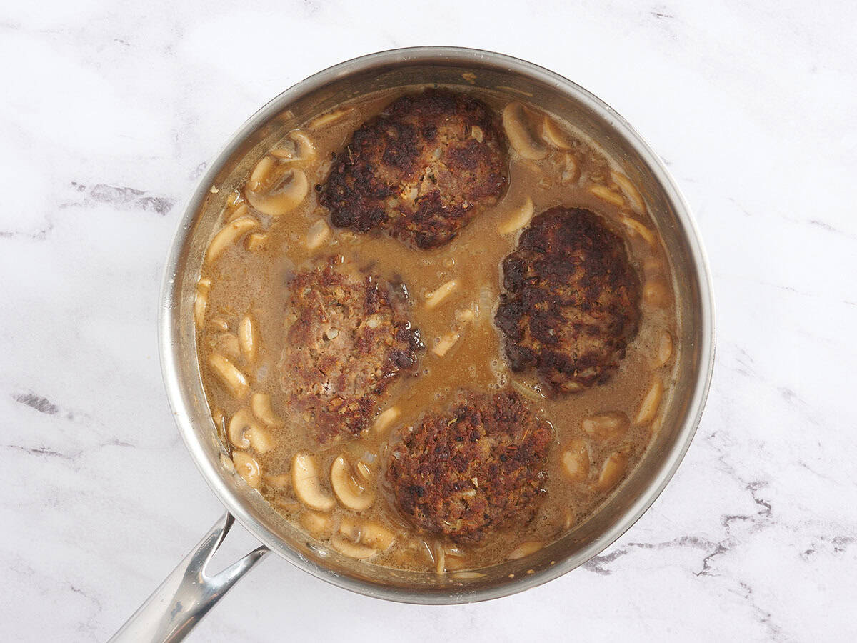Salisbury steak patties added to a skillet with gravy.