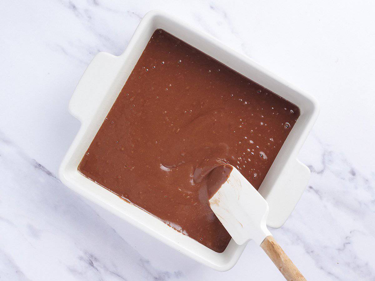 A spatula spreading the batter for chocolate depression cake in a baking dish.