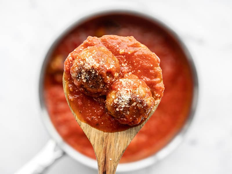 This simple recipe for Chicken Parmesan Meatballs is an easy weeknight dinner win! Swap out any ground meat you have for a quick and delicious dinner. BudgetBytes.com Two chicken Parmesan meatballs on a wooden spoon held above the pot of sauce.