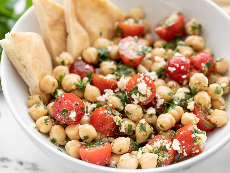 This super simple chickpea salad is bright and flavorful thanks to homemade chimichurri and feta. Goes great with all your summer grilling! BudgetBytes.com Close up side view of the bowl of Chimichurri Chickpea Salad with pita triangles in the side of the bowl