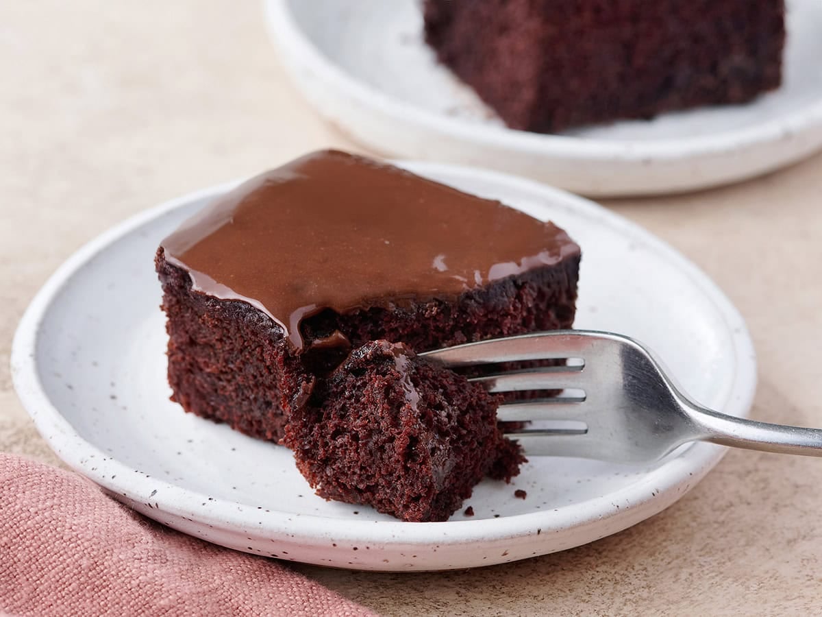 This unique Chocolate Cake recipe, popularized during the great depression, is rich and chocolatey without the using any eggs, butter, or milk! BudgetBytes.com A slice of homemade chocolate depression cake on a plate with a fork taking some.