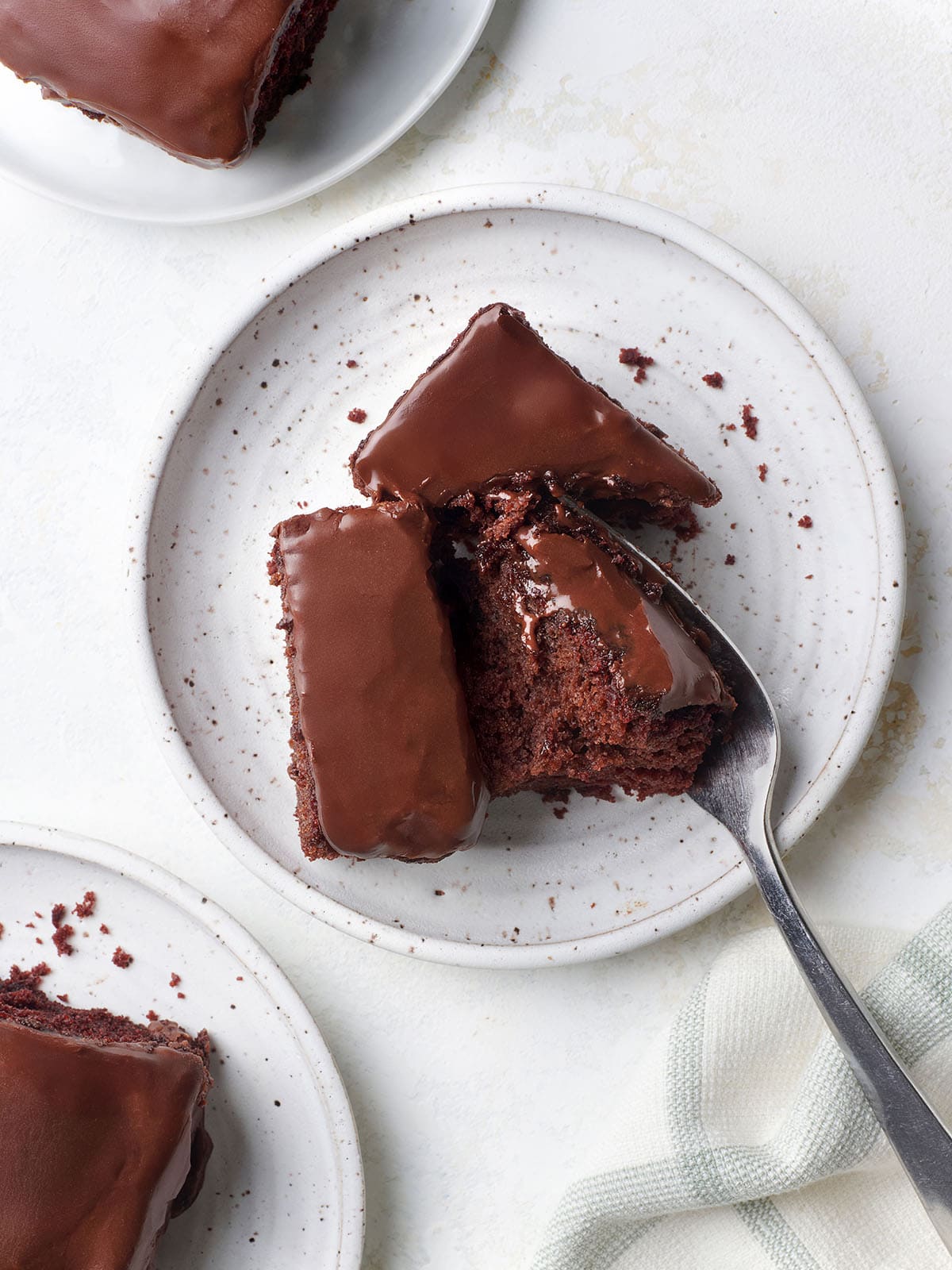 Overhead view of a slice of homemade chocolate depression cake, broken in half by a fork, on a plate.