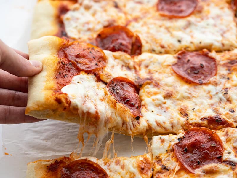 This quick and easy no yeast pizza dough only takes 15 minutes to make and is a great substitute for the classic when ingredients are in short supply. BudgetBytes.com A hand lifting one slice of pepperoni pizza out of the side, with cheese pulling between slices.