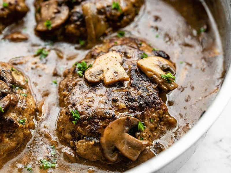 Homemade Salisbury Steak with a rich mushroom gravy is a quick, simple, and hearty weeknight dinner that will fill even the biggest of appetites! BudgetBytes.com Close up side view of the Salisbury Steak in the skillet with mushroom gravy.