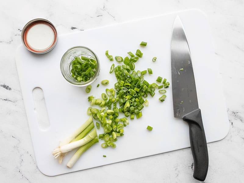 Learn how to store and freeze green onions to reduce waste, save money, and always have fresh green onions on hand for cooking! BudgetBytes.com Sliced green onion on a cutting board with a chef's knife and mason jar on the side