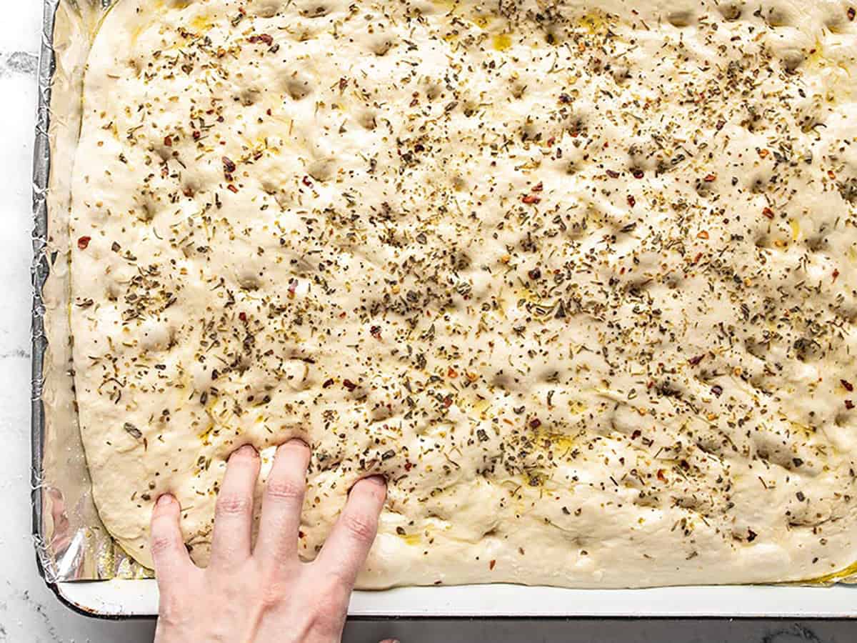 Fingers poking into the focaccia dough to make dimples.