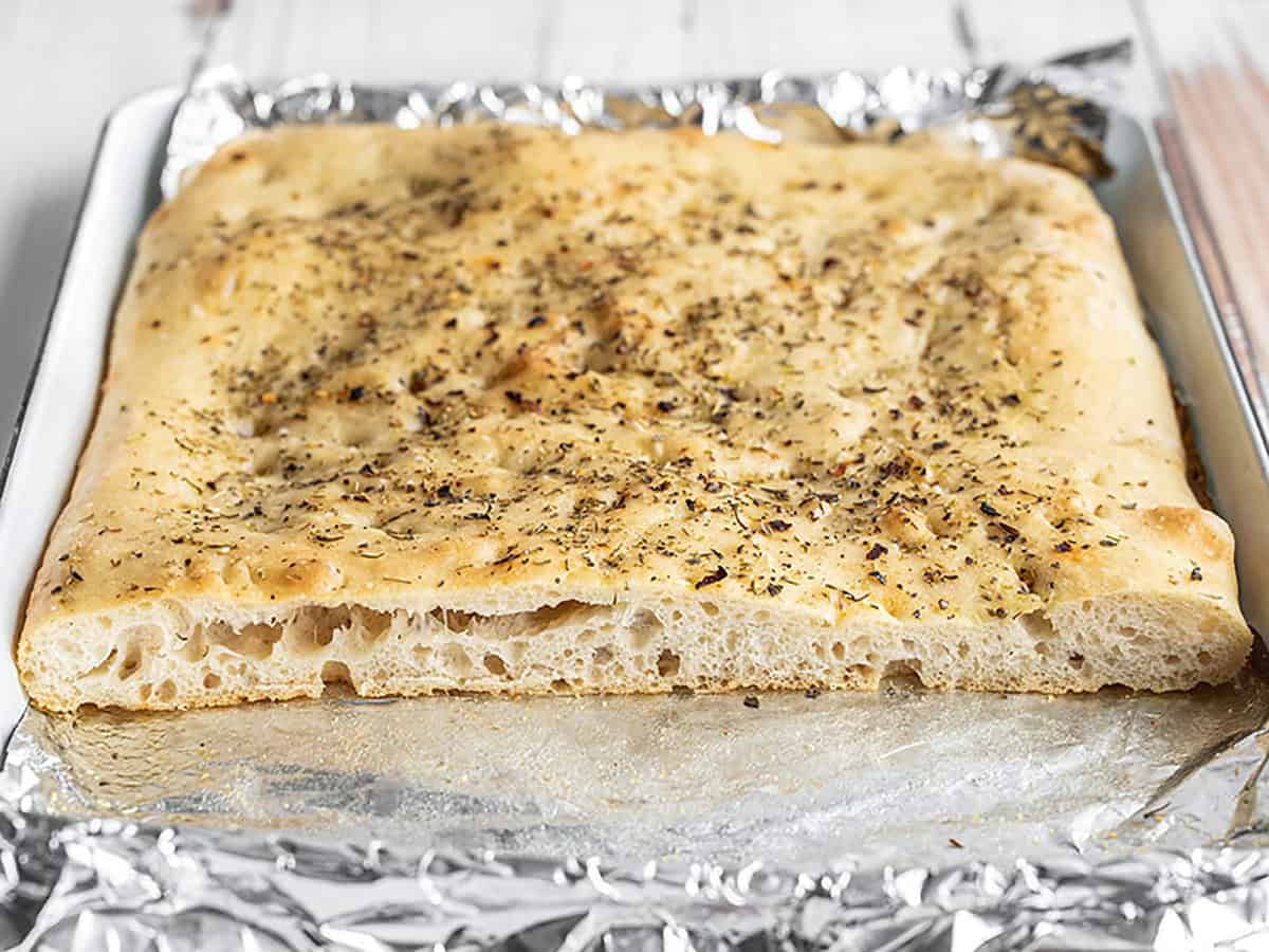 Focaccia bread on the baking sheet but cut open to show the internal bubbles.